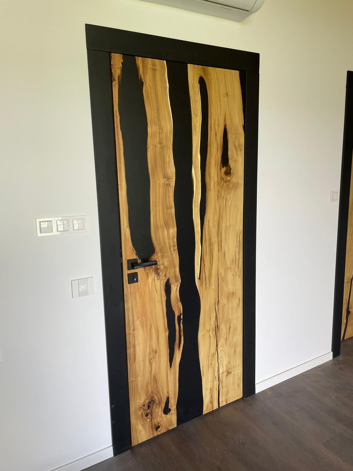 Prezentacja nowoczesnych drzwi wewnętrznych z litego drewna i czarnym wypełnieniem, jako przykładu unikatowego designu w aranżacji wnętrz.