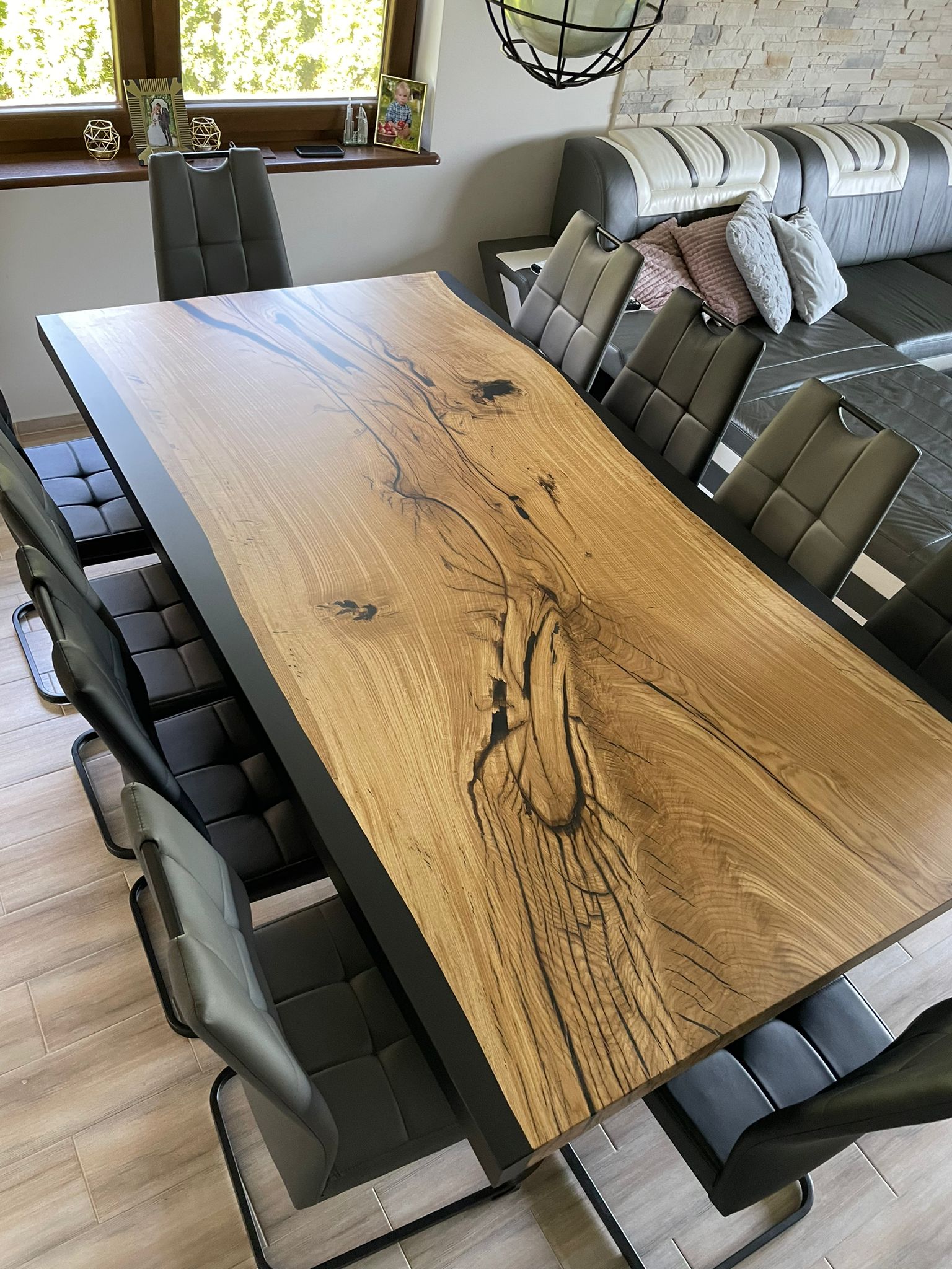 Prezentacja nowoczesnego stołu z litego drewna o widocznych słojach i pęknięciach, wypełnionych czarnymi akcentami, jako eleganckiego mebla w aranżacji salonu/jadalni.