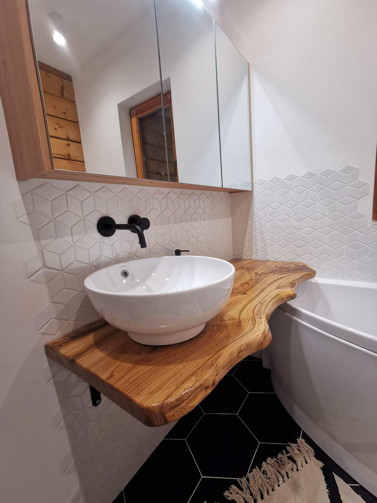 Prezentacja drewnianego blatu łazienkowego z naturalną krawędzią, na którym zamontowano umywalkę nablatową, jako przykładu nowoczesnej aranżacji w niewielkiej łazience.