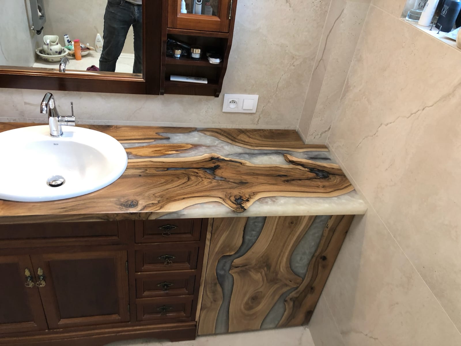 Prezentacja nietypowego blatu łazienkowego z litego drewna i jasnej żywicy epoksydowej, wkomponowanego w klasyczne szafki, jako przykładu oryginalnego designu w aranżacji łazienki.
