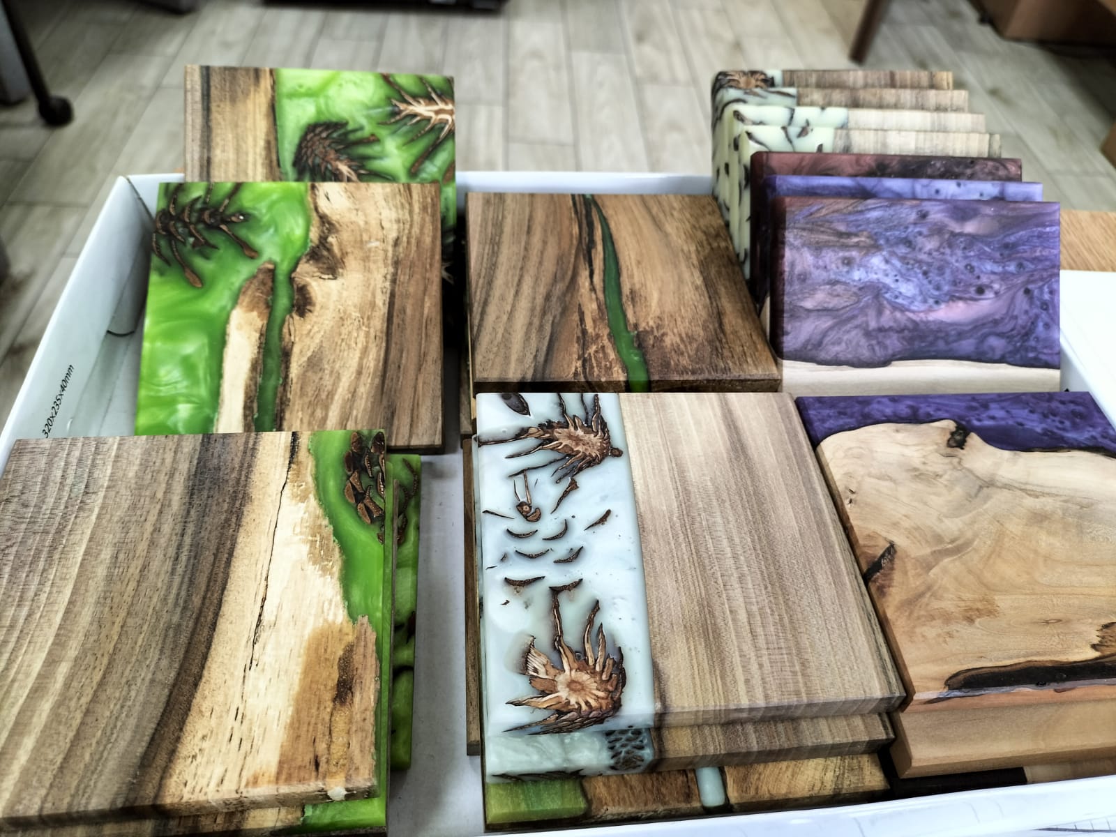 Prezentacja kolekcji ręcznie wykonanych podkładek z drewna i żywicy epoksydowej w różnych kolorach, jako praktycznych i dekoracyjnych akcesoriów do wnętrz.