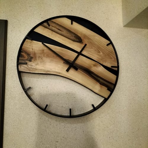 Prezentacja okrągłego zegara ściennego łączącego elementy litego drewna z metalową ramą, jako oryginalnego dodatku dekoracyjnego w aranżacji wnętrz.